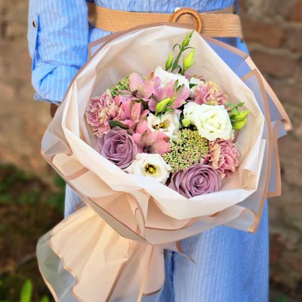 Buchet elegant de flori în nuanțe pastel, ținut de o persoană îmbrăcată în rochie albastră.