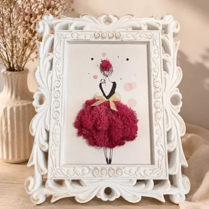 Tablou decorativ cu licheni naturali stabilizați, înrămat într-o ramă albă vintage, reprezentând silueta unei femei cu rochie roz realizată din licheni.