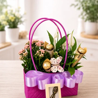 Coș cadou elegant cu plante în ghiveci, bomboane Ferrero Rocher și semn de carte decorativ, aranjat într-un suport roz cu fundă mov.