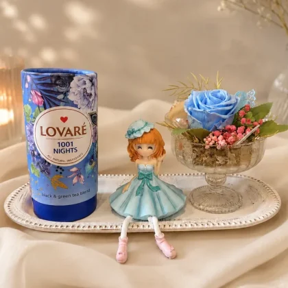 Pachet cadou cu ceai Lovaré 1001 Nights, aranjament floral cu trandafir albastru criogenat și figurină decorativă, prezentate pe tavă elegantă.