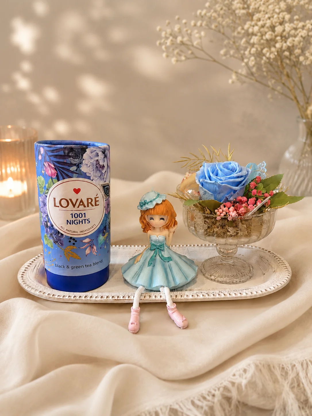 Pachet cadou cu ceai Lovaré 1001 Nights, aranjament floral cu trandafir albastru criogenat și figurină decorativă, prezentate pe tavă elegantă.